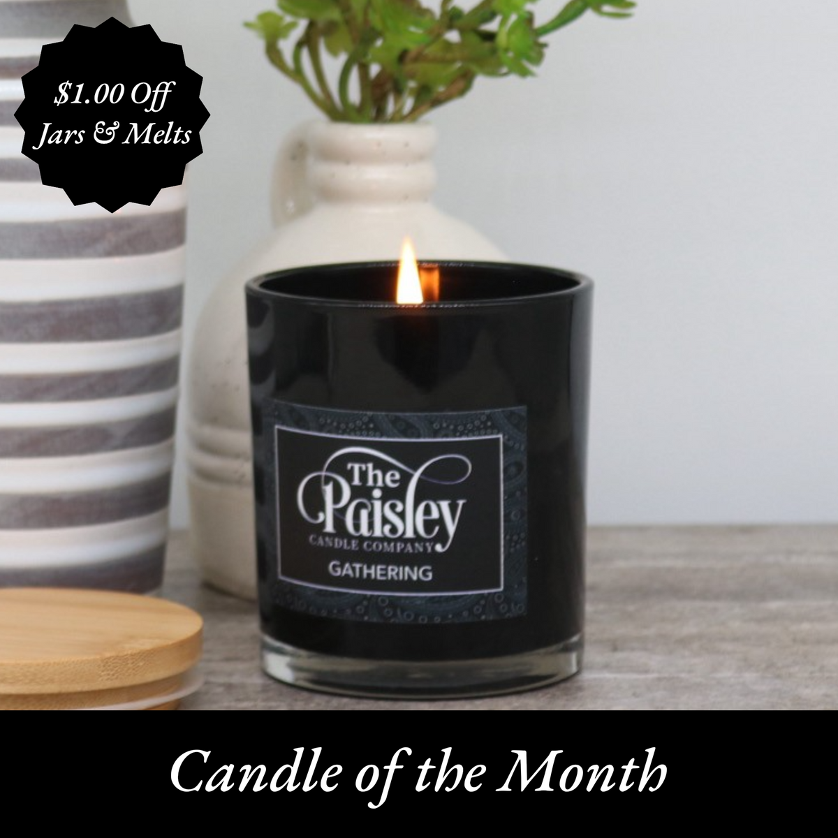 Black glass candle with wooden lid labeled 'The Paisley Candle Company – Fresh Cut Grass' placed beside a decorative faux grass sphere.