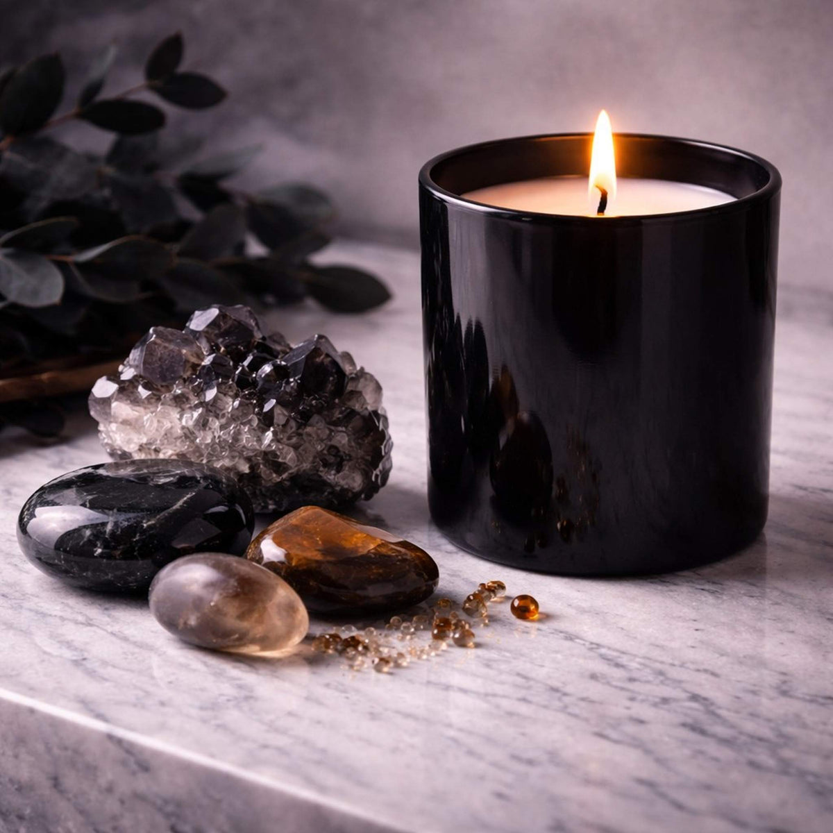 Black candle in luxury glass jar with amber crystals and dark botanical elements on marble surface