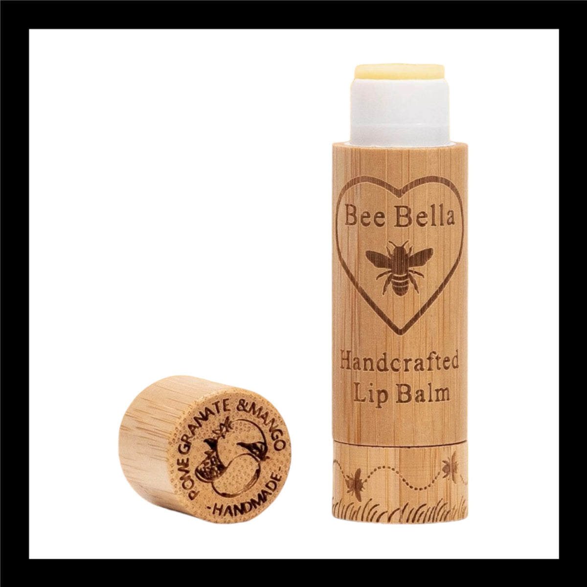 Bee Bella Handcrafted Lip Balm in eco-friendly bamboo packaging, featuring an engraved bee and heart design. The cap, placed beside the tube, is engraved with 'Pomegranate & Mango Handmade' alongside fruit illustrations.