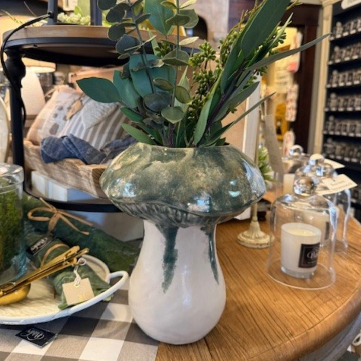 Ceramic mushroom vase displayed on a wooden table with lush greenery arranged inside. This 9" diameter x 10.5" tall vase serves as a stunning centerpiece, bringing a touch of nature-inspired charm to home decor.