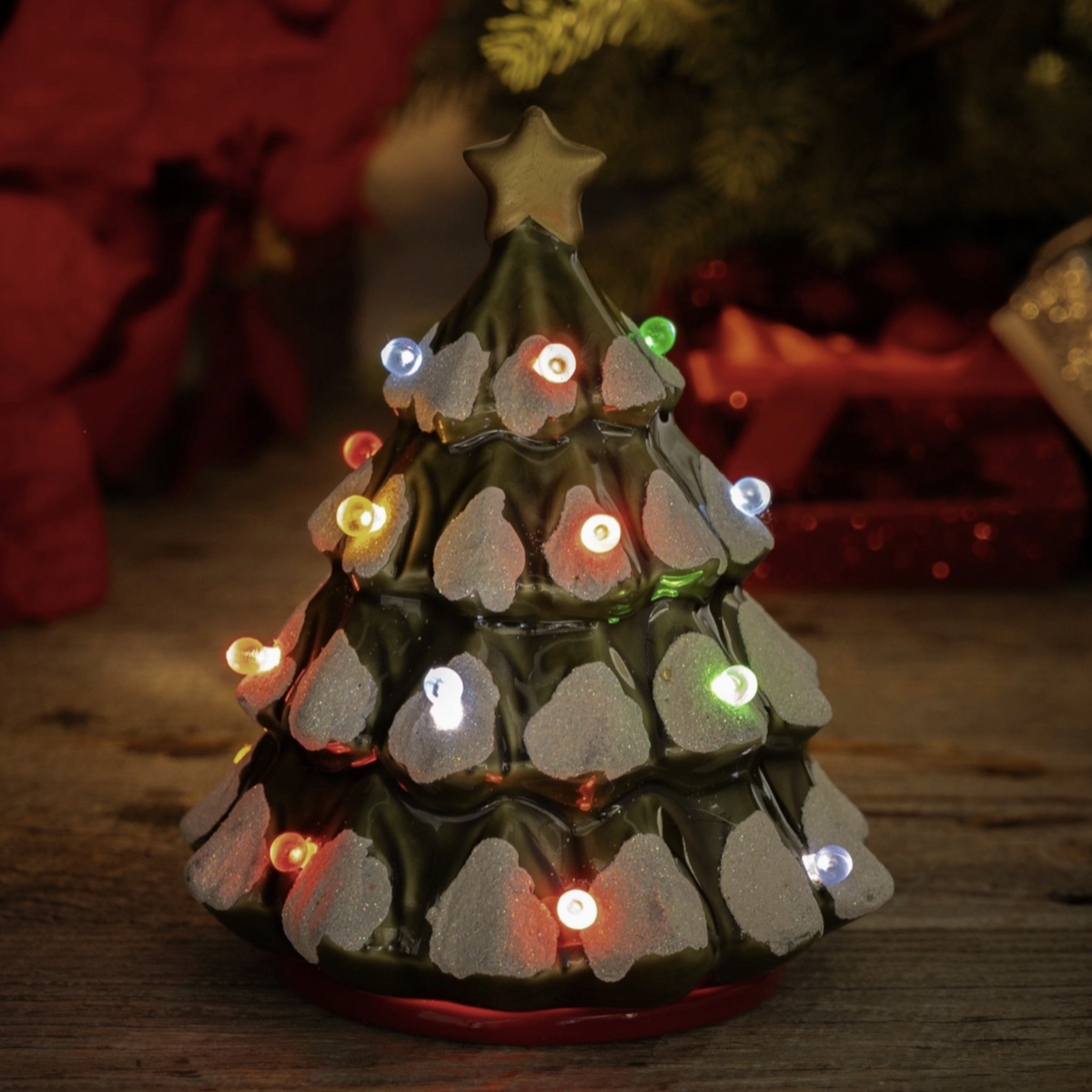 Decorative Christmas tree wax warmer with lights on a wooden surface, blurred festive background