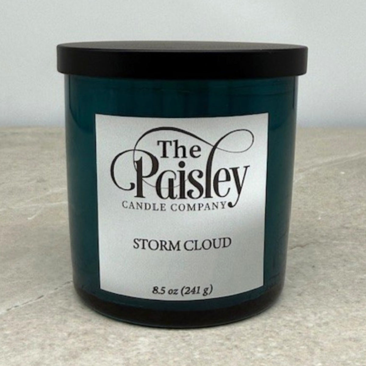 Storm Cloud candle by Paisley Candle Company in teal glass jar with black lid on neutral background